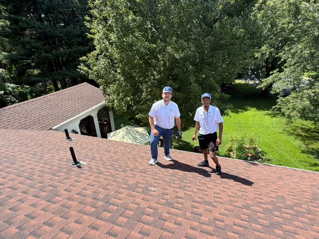 Two Eversafe Roofing estimators in branded polos and caps standing on a finished residential roof