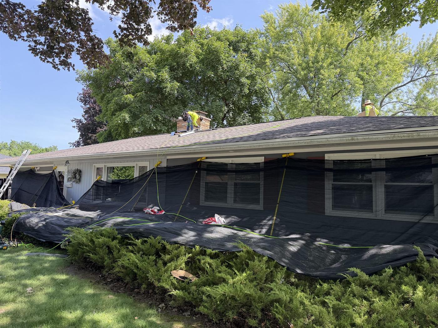 Eversafe Roofing crew protecting a home's siding and landscaping with tarps before a roof replacement