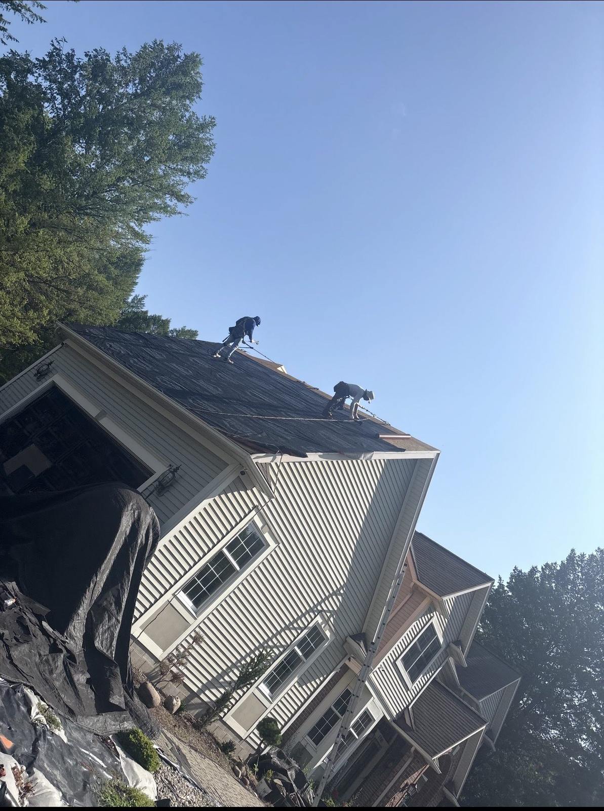 Roofers installing synthetic underlayment on a steep two-story roof