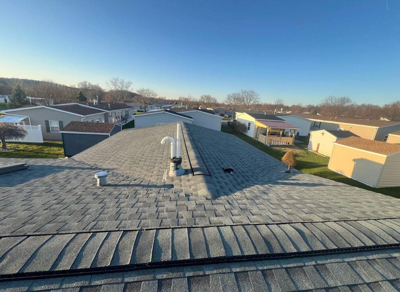 Completed gray architectural shingle roof with new ridge cap on a manufactured home at sunset