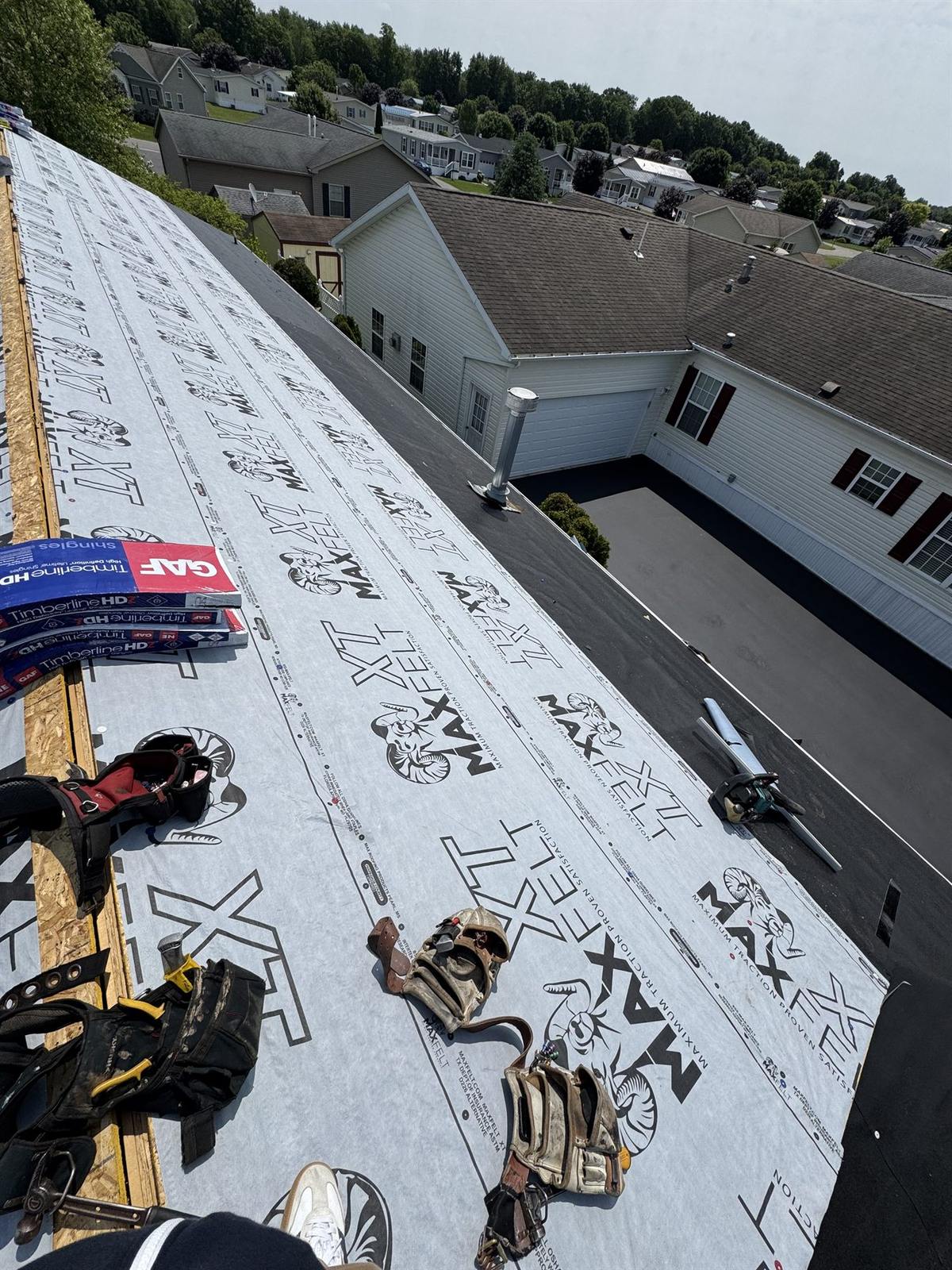 Roof deck covered in synthetic underlayment with GAF Timberline HDZ shingle bundles staged for installation
