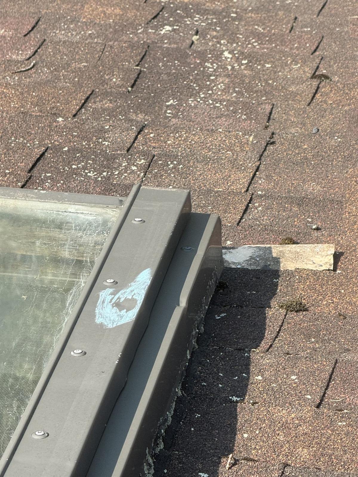 Chalk-circled hail impact on skylight flashing with granule loss and lifted shingle edges on a storm-damaged asphalt roof