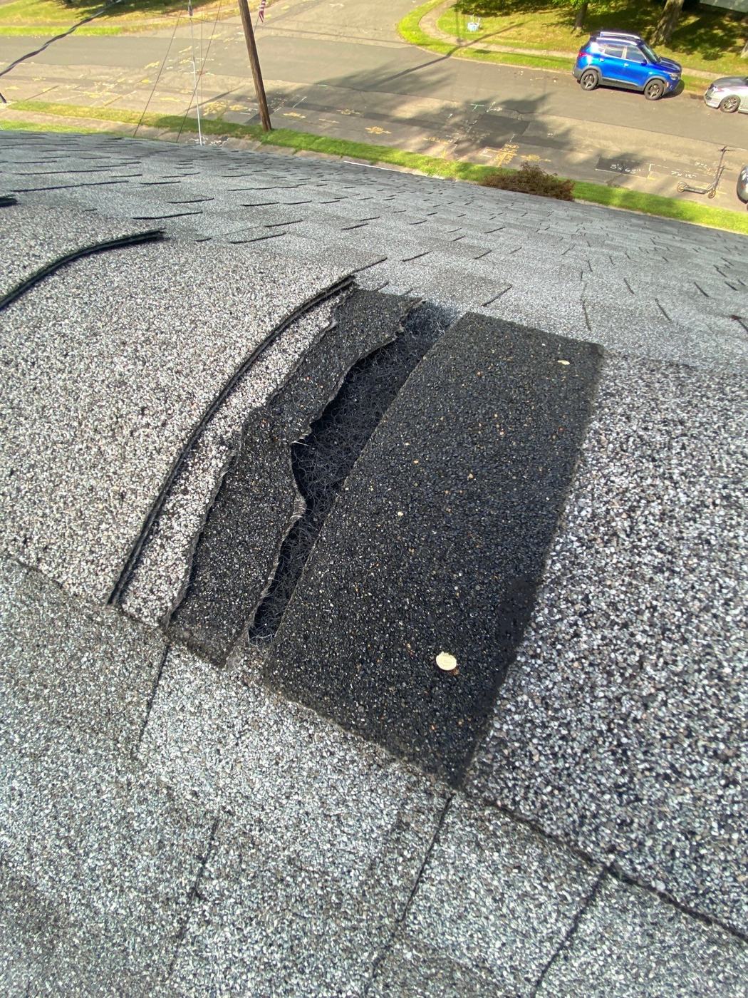 Shingles torn away from a roof hip by wind, exposing the underlayment and course beneath