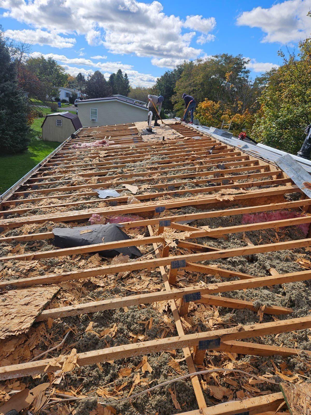 Roof stripped to bare rafters showing rotted, disintegrated wood decking before deck replacement